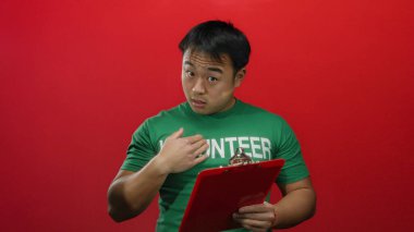 Yeşil gönüllü gömlekli Asyalı genç adam, elinde kırmızı bir arkaplan var.