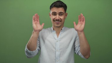 Genç İspanyol adam, bu dinamik çerçevelerde izole edilmiş yeşil bir arka plan duvarına gülümserken, duygularını ve etkileşimlerini vurgulayarak, şakacı bir şekilde gözlerini örtüyor ve açıyor..