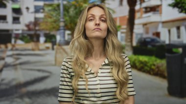 Sokakta sarı saçlı, açık havada dikilen kadın gündüz vakti şehir bölgesinde çizgili gömlek giyiyor..