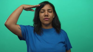 Yüzü önde olan Afro-Amerikalı kadın stüdyoda selam veriyor yeşil perde arkası ve mavi gömlekli; saygı.