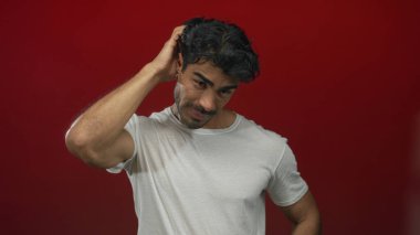 Beyaz tişörtlü bir adam kırmızı bir stüdyo ortamında kafasını kaşıyordu. Şaşırmış bir bakışla aşağıya bakıyordu..