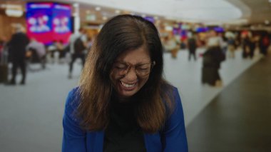 Orta yaşlı mavi ceketli kadın gözlüklü gülüyor ve havaalanı terminalinde dişlerini gösteriyor. Mutluluk..