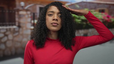 Kırmızı tişörtlü kadın, gün ışığında ciddi bakışlarla girişte selam veriyor; saygı..