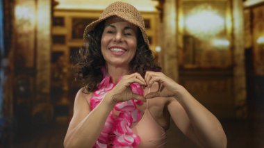 Bikinili orta yaşlı bir kadın ve Hawaii zambağı kilisede elleriyle kalp şekli oluşturur..