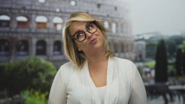 Genç sarışın kadın dudaklarını büzüyor ve dışarıdaki Roma binasının önünde gözlük takıyor..