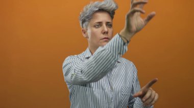 İşaret parmağını diğer eliyle turuncu stüdyo arka planına doğru uzatan kadın, konsantrasyon belirleme odağı.