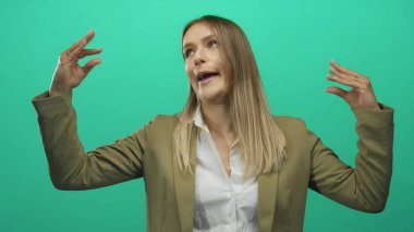 İzole edilmiş yeşil arkaplan karşısında el kol hareketi yapan kadın spor ceket ve beyaz gömlek giyip iletişim ve ifade öneriyor..