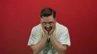 Sakallı ve steteskoplu genç bir doktor, izole edilmiş bir stüdyoda canlı kırmızı bir arka plan karşısında şaşkınlığını dile getiriyor..