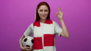 Futbol topu takan kadın pembe arka planda onay işareti gösteriyor, destek ve mutluluk gösteriyor..