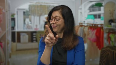 Orta yaşlı, mavi ceketli, parlak bir giyim mağazası koridorunda sırıtırken göğsünü gösteren İspanyol bir kadın..