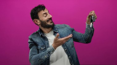 Sakallı bir adam arabanın anahtarlarını tutarken gülümsüyor.