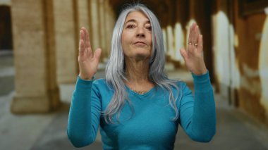 Eski bir üniversitenin açık hava koridorunda elleri dramatik bir şekilde kır saçlı, turkuaz süveter giyen son sınıf öğrencisi bir kadın..