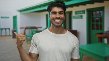 Güneşli bir günde beyaz saray girişinde arkasında başparmağını gösteren İspanyol genç adam sıcak karşılama.