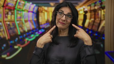 Orta yaşlı İspanyol kadın kumarhanedeki parlak kumar makinesinin yanında yanakları işaret ediyor..