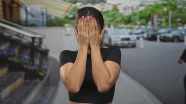 Siyah mahsul bluzu giyen genç sarışın kadın, park yeri kaldırımında el hareketini durdurmak için avuçlarını kaldırıyor..