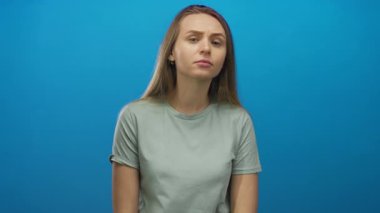 Canlı mavi bir arka plana karşı gelişigüzel giyinmiş bir kadın, izole edilmiş bir stüdyo ortamında merak ve içgözlem duygusu taşıyor..