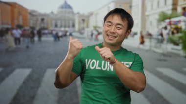 St. Peter Meydanı, Vatikan 'da yeşil tişörtle gülümseyen gönüllü genç adam pozitifliğini ve nişanını ifade ediyor..