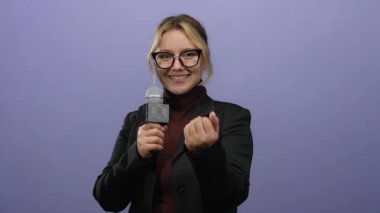 Mikrofonlu ve hareketli bir kadın muhabir gözlüklü ve takım elbiseli mor bir arka planda buraya gelir..