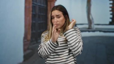 Dışarıdaki kadın şaşırmış görünüyor. Yüzünde çizgili tişört, sarı saç ve bulanık şehir geçmişine karşı endişeli bir ifade var..