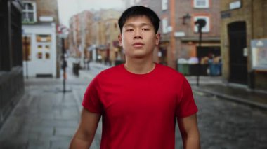 Şehir sokaklarında kırmızı gömlekli genç adam, şehir mimarisi ve kaldırım kaldırımlarının bir zeminine karşı duygularını ifade ederek, hareketli bir açık hava sahnesi yakalıyor..