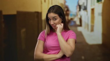 Pembe tişörtlü bir kadın, güneşli bir sokakta gülümsüyor. Bulanık binalar, açık hava eğlencesi ve dostça davranışlar sergiliyor..