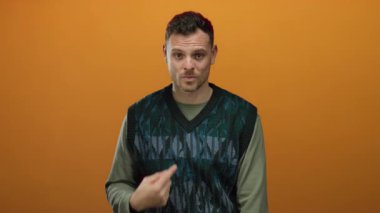 İspanyol bir adam, kendini izole edilmiş turuncu bir arka plana işaret ediyor. Kafası karışıklığı ve belirsizliği, genç ve anlamlı bir davranışı gösteren el hareketleriyle ifade ediyor..