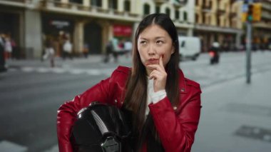 Kırmızı ceketli kadın, canlı bir açık hava sahnesinde şehir hayatı tarzını ve düşünceli ifadesini sergileyen miğfer taşıyan hareketli şehir caddesini düşünüyor..