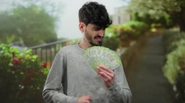 Açık hava parkı ortamında hüzünlü bir ifadeyle Rus ruble banknotları tutan adam, doğal bir arkaplanda mali rahatsızlığı vurguluyor..