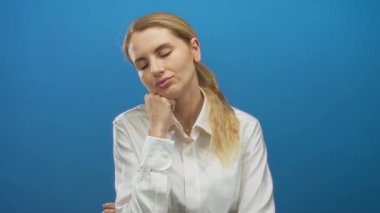 Mavi arka planda beyaz gömlek giyen bir kadın minimalist stüdyo ortamında yorgunluk hissini canlandırıyor..