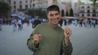 Zeytin yeşili kazaklı adam kalabalık şehir caddesinde elleri havada ve gülümseyen yüzüyle dans eder; mutluluk.