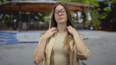 Yumuşak güneş ışığı altında, yemyeşil parkta, ahşap pavyonun yanında uzun sarı saçlı bir kadın takla atar..