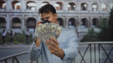 Roma Kolezyumu 'nda elinde kamera ve dolar banknotları tutan genç adam eğlence amaçlı seyahat finans ve fotoğrafçılığı ön plana çıkarıyor..
