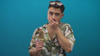 Mavi arka planda renkli tişörtlü dondurma külahını tutan genç bir adam şaşkınlığını dile getiriyor.