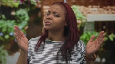 Surat ifadesini sorgularken duvarın önünde elleri olan boş bir alanı çerçeveleyen kadın; tereddüt karmaşası.