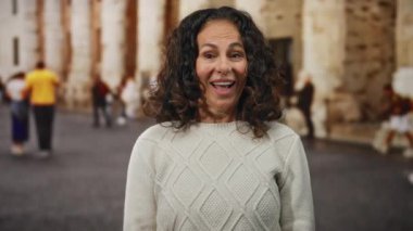 Kıvırcık saçlı İspanyol kadın, şehir dışındaki bir sokak sahnesinde mutsuzluktan mutluluğa dönüşüyor. Havayı, ilişkilendirilebilir duygularla dolduruyor..