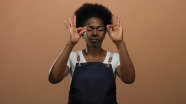 Önlük giyen kadın meditasyon jesti yapıyor izole edilmiş kahverengi arka plana karşı duruyor barış ve konsantrasyon yayıyor..