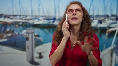 Deniz kenarında, açık gökyüzü altında teknelerle gülümseyen telefonlu bir kadın güneşli bir günde okyanus kenarında neşeli bir ifade sergiliyor..