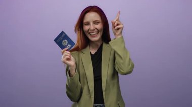 Gülümseyen kadın mor arka planda Kore pasaportu tutuyor, kutlama yaparken heyecan ve sevinç ifade ediyor, yeşil bir ceket giyiyor ve parmağıyla yukarı işaret ediyor..