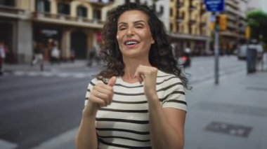 Kadın, bulanık şehir binaları ve trafiğinin ortasında başparmağıyla omzunun üstünden bakıyor; kendine güven.