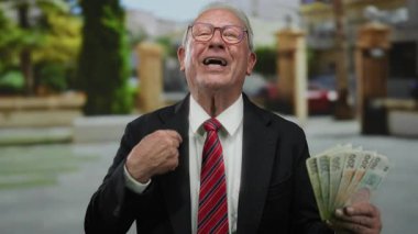 Son sınıf öğrencisi elinde Czech Koruna banknotları tutarak şevkini ifade ediyor, zenginliğini sergiliyor, yeşillik ve bulanık şehir geçmişi olan bir iş ortamında yer alıyor..