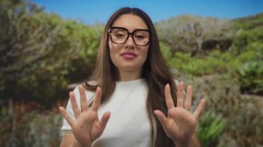 Kaşlarını çatan ve burnunu kırıştıran gözlüklü genç İspanyol kadın ormanda ellerini kaldırarak iğreniyor..
