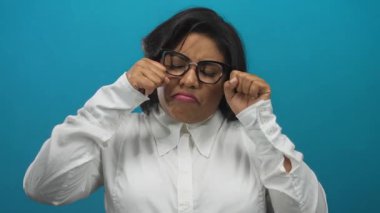 Beyaz gömlekli genç bir kadın, mavi duvara karşı ağlıyor. Duygularını ve mizahını dışa vuruyor..