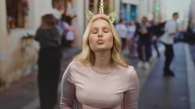 Tek boynuzlu at takan genç bir kadın işlek bir şehir caddesinde şakacı jestler yapıyor, açık hava kentsel gökyüzünün altında sarı saçları ve diyademiyle tuhaf bir sahne oluşturuyor..