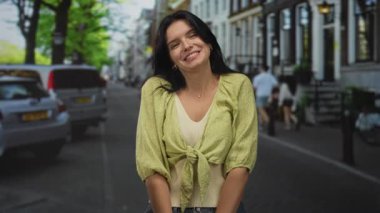 Kadın başını hafifçe eğiyor. Yüzü, park etmiş arabaları ve yeşil ağaçları olan yapraklı bir caddede beliren bir gülümseme. Huzur neşesi..