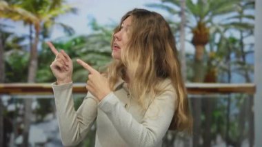 Kadın parmağı, balkon sarışını işaret ediyor. Palmiye ağaçları tarafından şaşırtılıyor. Tropikal pencere manzarası dikkat çekiyor..