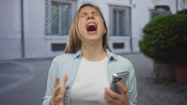 Dışarıdaki kadın, şehir ortamında elinde telefonla, gün ışığında duygu ve tepki gösteren bitkilerle hayal kırıklığını ifade ediyor..