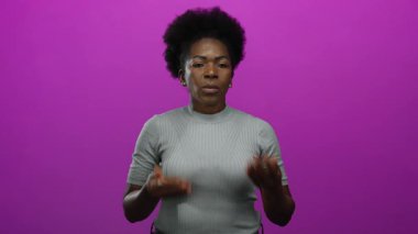 Afro saçlı bir kadın pembe arka planda ellerini sallayarak neşeli bir jest yaparak rahatlıyor.