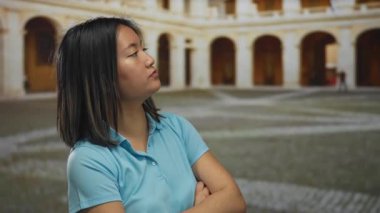 Eski üniversite binasının avlusunda güvenle poz veren Çinli kadın kemerli mimari ve yıpranmış taşla, gençlik kararlılığı ve akademik takibi ile.