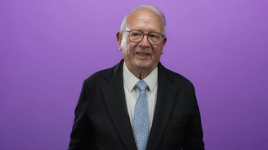 Tecrit edilmiş mor arkaplana karşı iş elbisesi içinde gülümseyen kıdemli adam çeşitli duyguları hoş bir tavırla ifade ediyor, kendine güveni ve pozitif enerjiyi somutlaştırıyor..