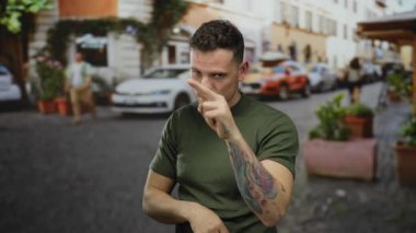 Canlı bir şehir caddesinde hareketli bir jest yapan İspanyol dövmeli genç adam, hareketli şehir hayatı arasındaki gözlem ve farkındalığı vurguluyor..